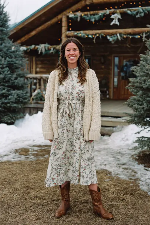 A woman over 30 wears a floral print high-neck dress with a cable-knit cardigan and brown cowboy boots