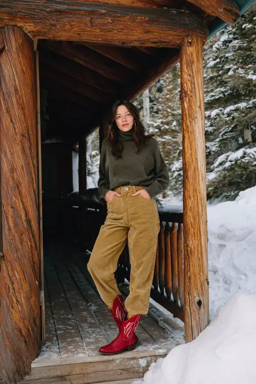 A woman over 30 wears high-rise corduroy pants with a relaxed pullover and short red cowboy boots