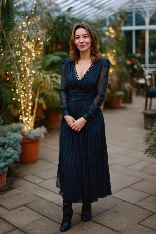 A woman over 40 wears a dark blue pleated chiffon gown with a beaded neckline and heeled boots