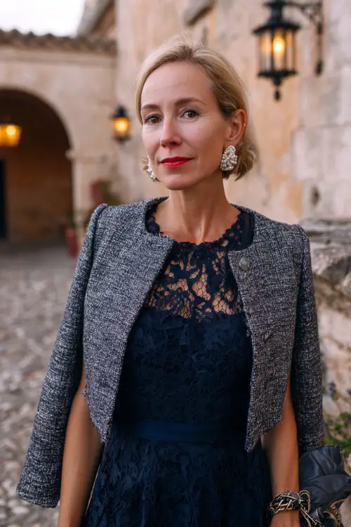 A woman over 40 wears a navy lace dress with a fitted gray tweed jacket