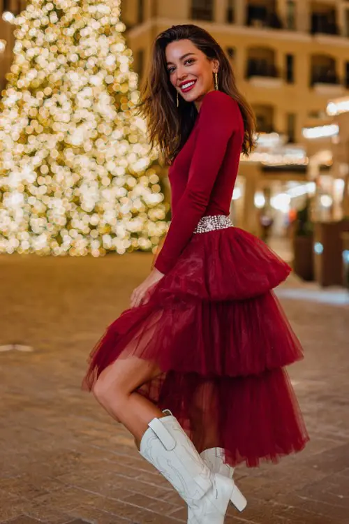 A woman wears a tiered tulle skirt with a red long-sleeve fitted top and pearl-detailed white cowboy boots