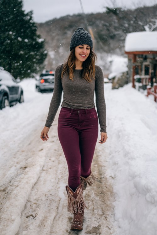 A woman wears burgundy leggings with fringe-trimmed cowboy boots, a fitted pullover, and a beanie