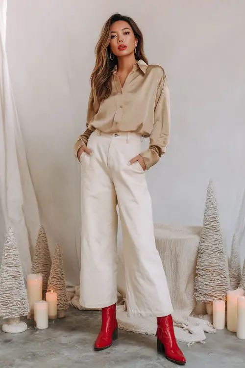 A woman wears off-white wide-leg trousers with a tucked-in camel satin blouse and red cowboy boots