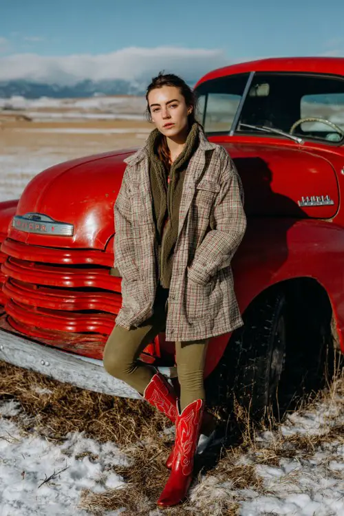 A woman wears olive green leggings with a longline flannel shacket and red cowboy boots