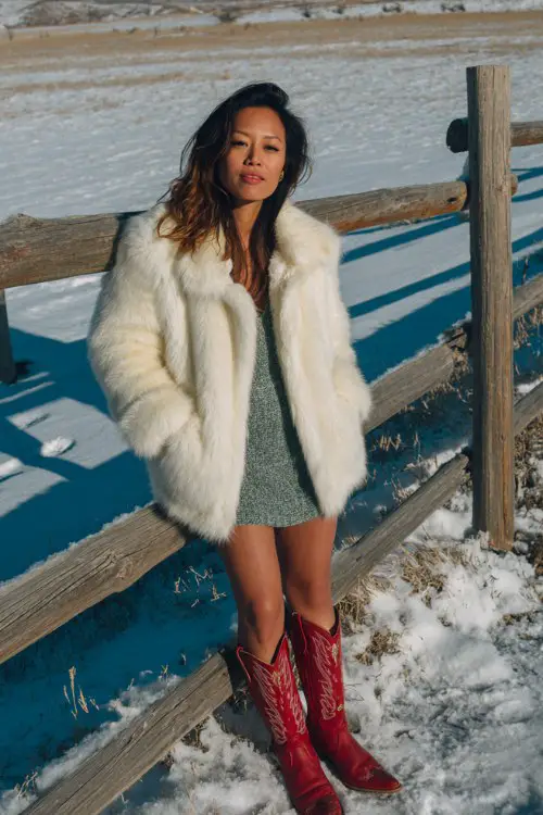 a woman wears a green dress with a white coat and red cowboy boots