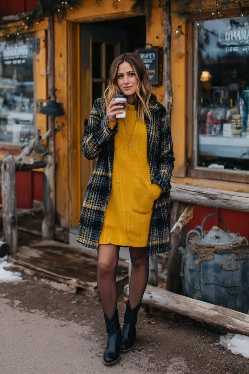 a woman wears a mustard sweater dress and a plaid coat and black cowboy boots