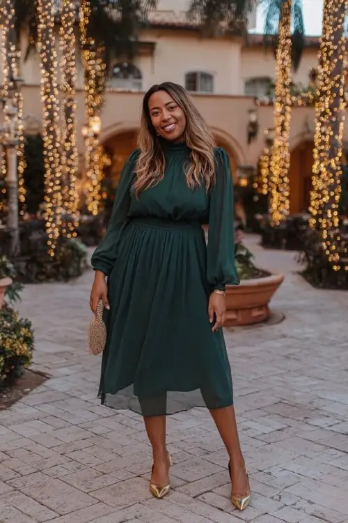 A curvy woman over 40 wears a dark green high-neck chiffon dress with flowy sleeves and gold pumps