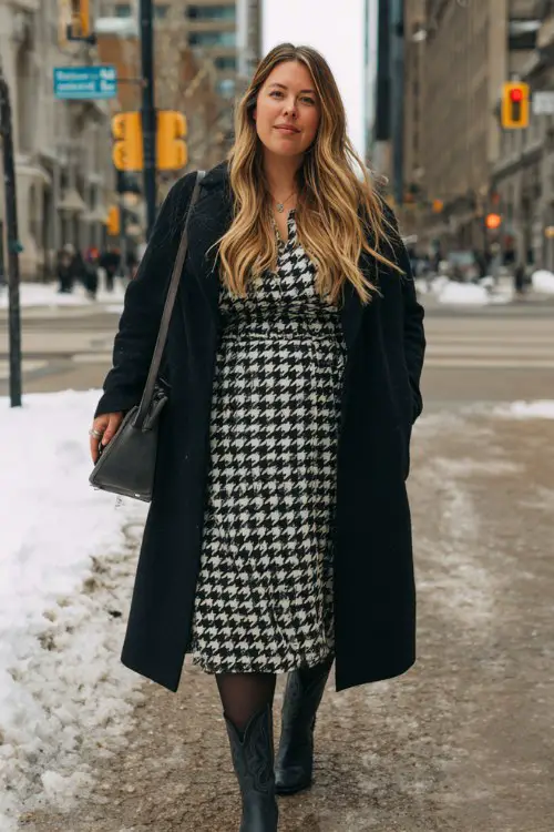 A plus-size woman wears a houndstooth print midi dress with opaque black tights and sleek black cowboy boots, layered with a long black wool coat