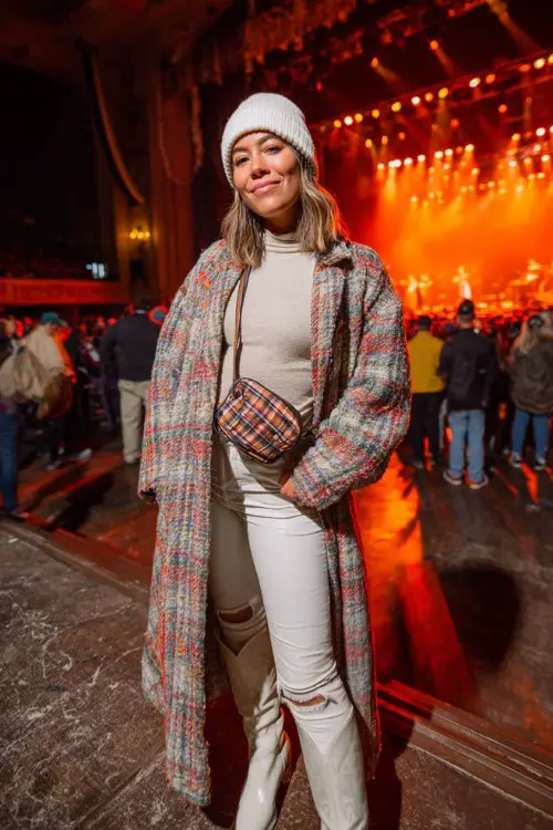 A plus-size woman wears white cowboy boots with faux-leather leggings, a fitted turtleneck and oversized plaid coat, styled with a beanie and crossbody bag
