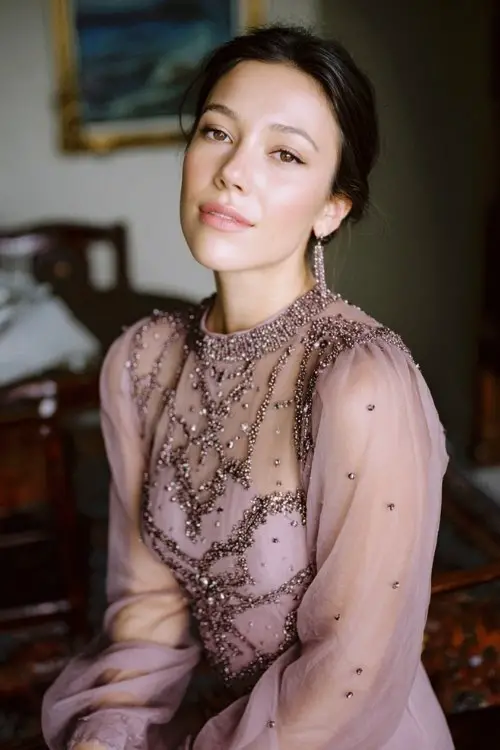 A woman framed in a pale mauve gown with sheer sleeves, hand-sewn beadwork, with sheer beaded sleeves