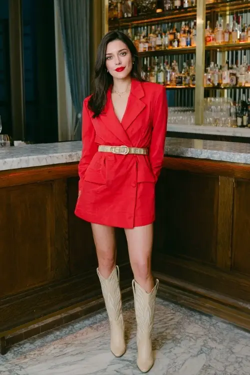A woman in a structured red blazer dress cinched with a belt, beige cowboy boots