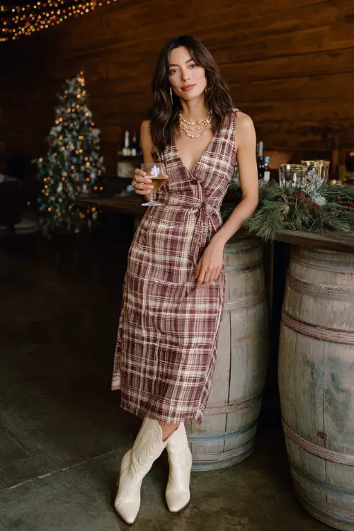 A woman over 30 wears a festive plaid midi dress with refined tailoring, paired with cream cowboy boots and pearl accessories