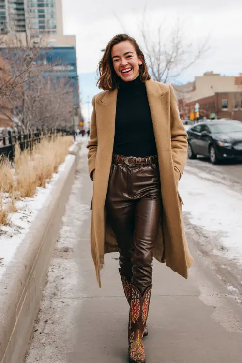 A woman over 30 wears faux leather leggings tucked into embroidered cowboy boots, a fitted turtleneck, and a belted wool coat