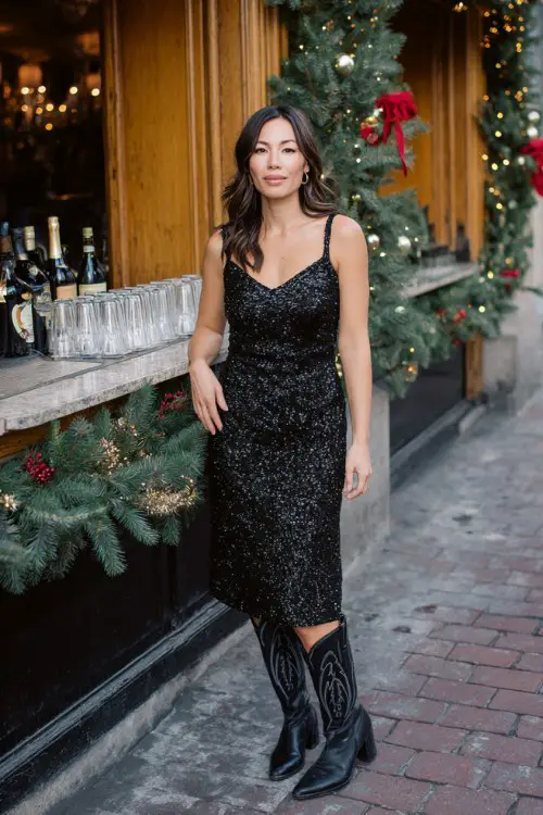 A woman over 40 wears a black sequin midi dress with subtle sparkle, paired with sleek black cowboy boots