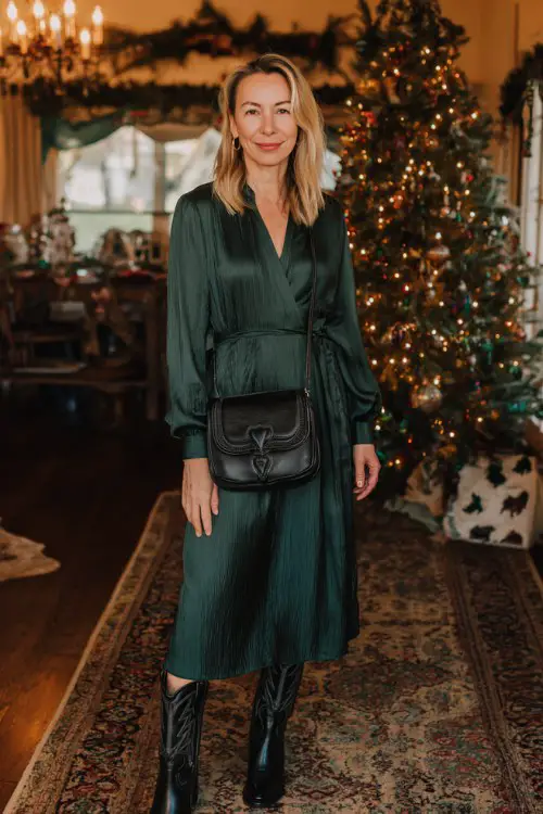A woman over 40 wears a forest green long-sleeve dress with elegant texture, paired with black cowboy boots and a structured shoulder bag