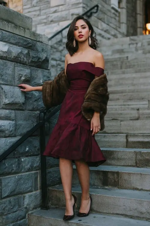A woman walking up stone steps in a rich burgundy off-the-shoulder dress with a fitted bodice and flared hem