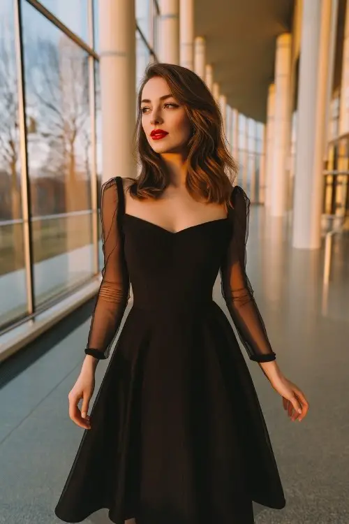A woman wears a black fit-and-flare cocktail dress with sheer mesh sleeves and red lips