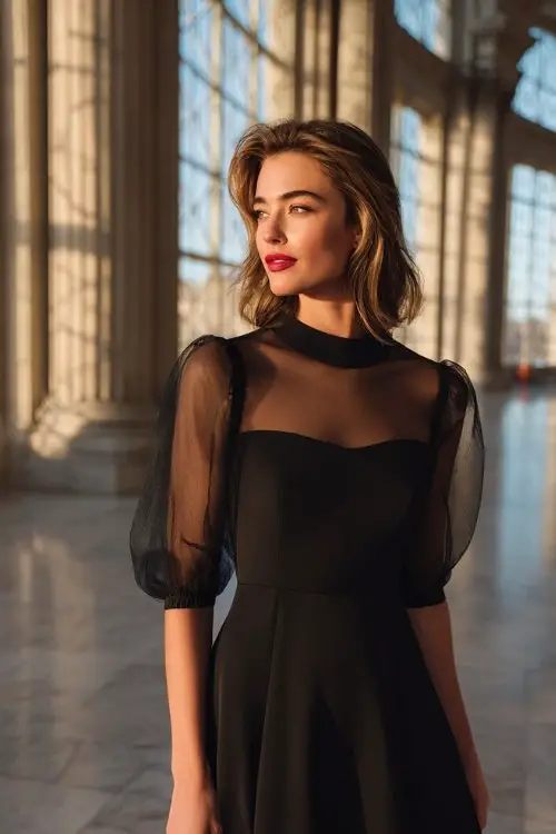 A woman wears a black fit-and-flare cocktail dress with sheer mesh sleeves and red lips