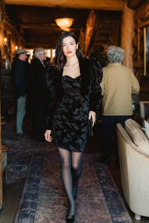 A woman wears a black jacquard floral dress with puff sleeves, paired with a velvet cropped jacket, sheer black tights, and Mary Jane heels