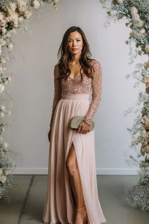 A woman wears a blush-toned long-sleeve gown with beaded embellishments and a flowing chiffon skirt