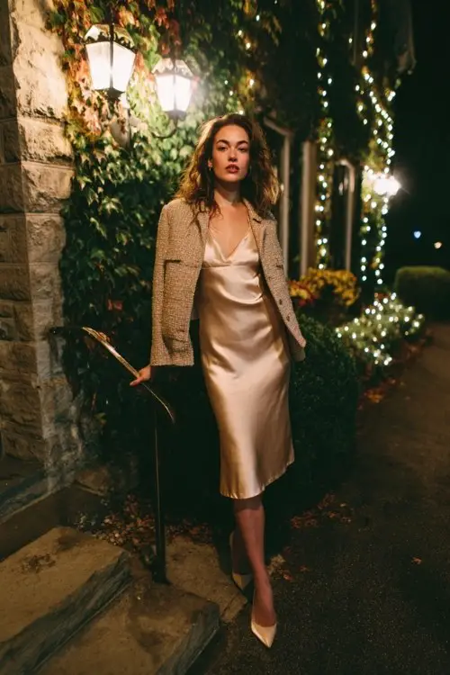 A woman wears a champagne satin slip midi dress with a cropped tweed jacket and pointed heels