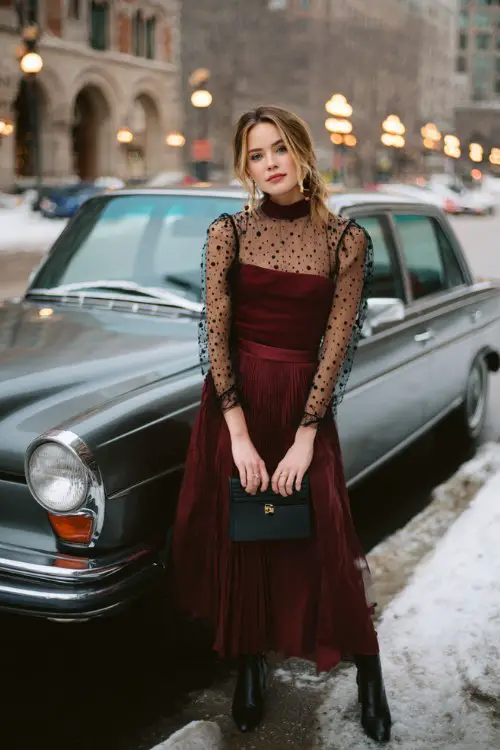 A woman wears a high-neck burgundy dress with sheer polka-dot sleeves and a pleated skirt