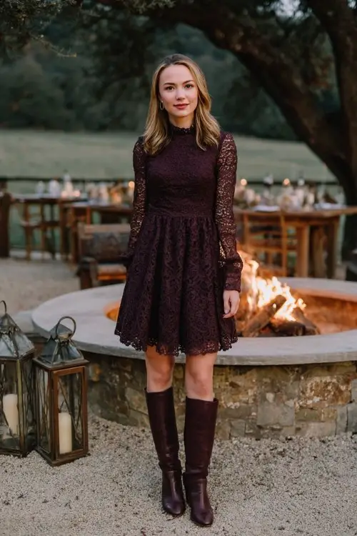 A woman wears a plum lace dress with full sleeves and a flared hem, paired with burgundy leather boots, standing near a fire pit at an outdoor winter wedding