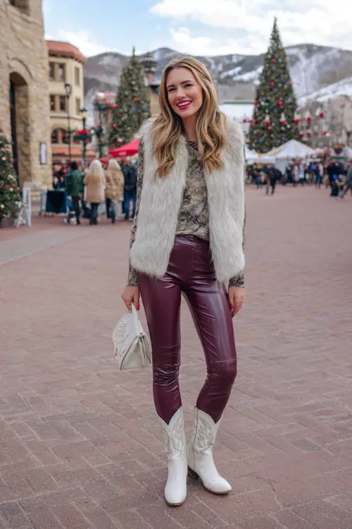 A woman wears burgundy leggings tucked into white cowboy boots, paired with a faux fur vest and a thermal long sleeve top
