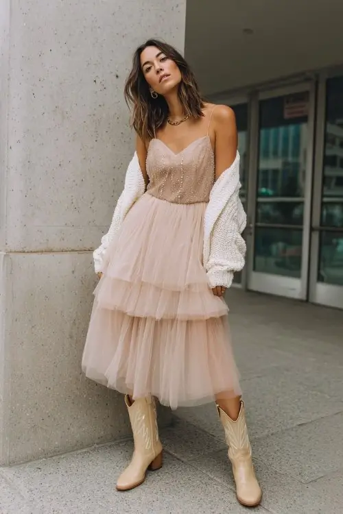 woman in a blush tulle midi dress with sparkly accents, layered with a cropped cream cardigan and beige cowboy boots for a soft party look