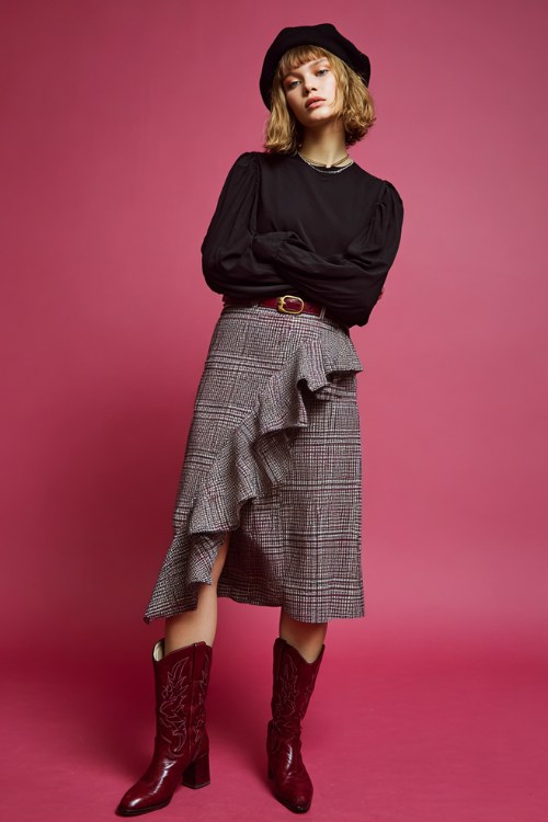 woman wearing black long sleeve blouse tucked into asymmetrical plaid midi skirt with ruffle detail, glossy burgundy cowboy boots, wide belt, black beret