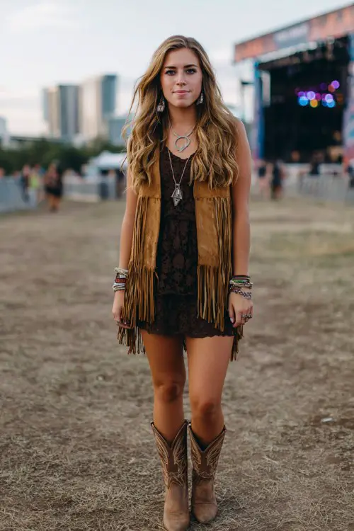 A bold country concert look featuring a lace mini dress layered with a suede fringe vest, western boots, stacked bracelets