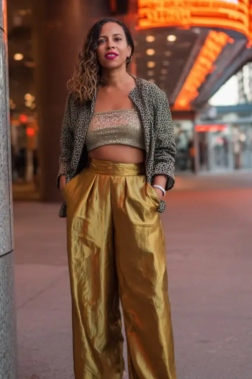 A curvy woman over 40 wears wide-leg trousers, a metallic knit top, and a cropped jacket