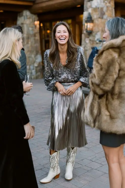 A woman in a metallic pleated skirt and embellished blouse, wearing ivory cowboy boots