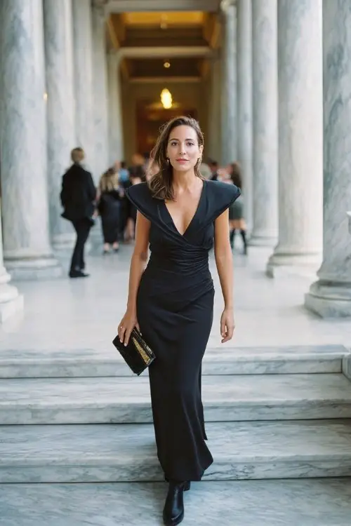 A woman over 30 wears a classic floor-length navy gown with structured shoulders, styled with stiletto-heeled black boots and a clutch