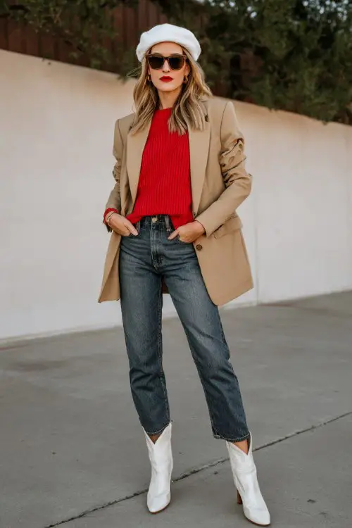 A woman over 30 wears a red crewneck sweater tucked into dark denim, topped with a tailored camel blazer, white cowboy boots
