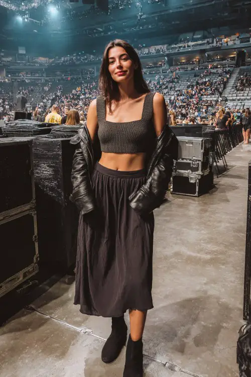 A woman wears a flowy midi skirt with a knit top and a cropped moto jacket, paired with sleek booties