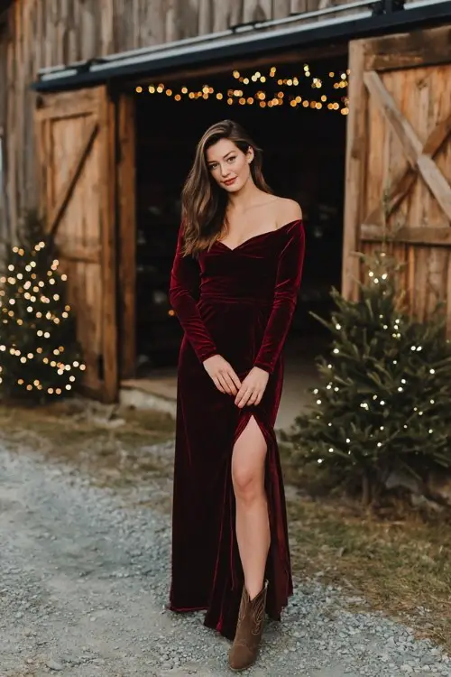 A woman wears a long-sleeve wine-red velvet gown with a subtle slit and sweetheart neckline, styled with ankle cowboy boots and a faux fur wrap
