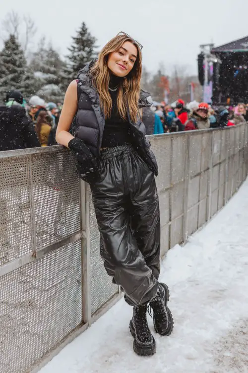 A woman wears faux leather joggers with a fitted turtleneck and puffer vest, paired with platform sneakers