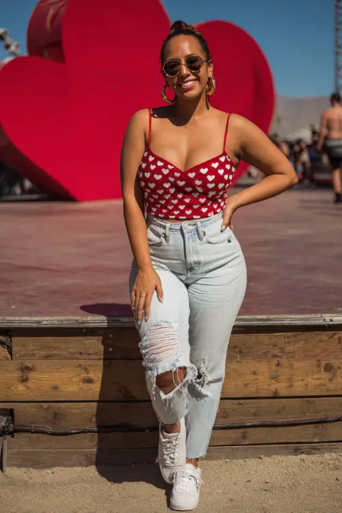 A curvy woman wears a fitted sequin heart-print top with high-waisted ripped jeans, white platform sneakers, and hoop earrings