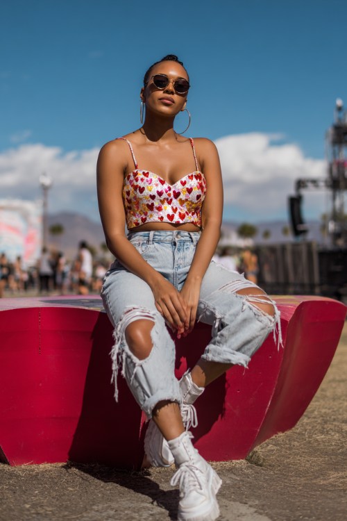 A curvy woman wears a fitted sequin heart-print top with high-waisted ripped jeans, white platform sneakers, and hoop earrings