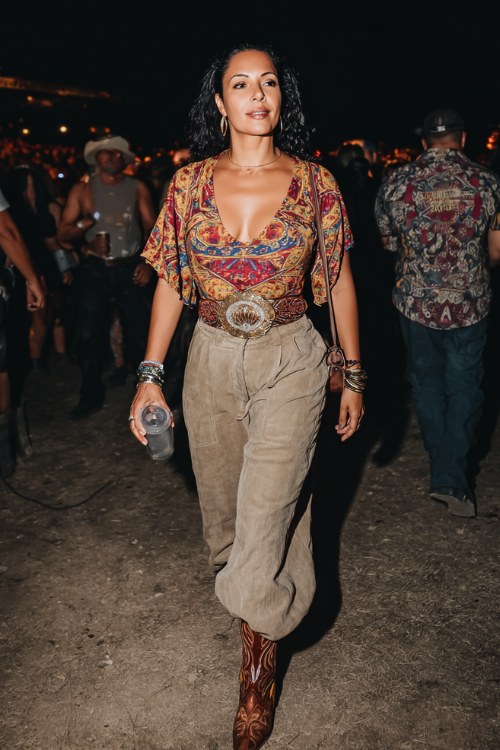 A curvy woman wears wide-leg trousers with a bold western print top and a statement belt, paired with heeled cowboy boots and layered bracelets