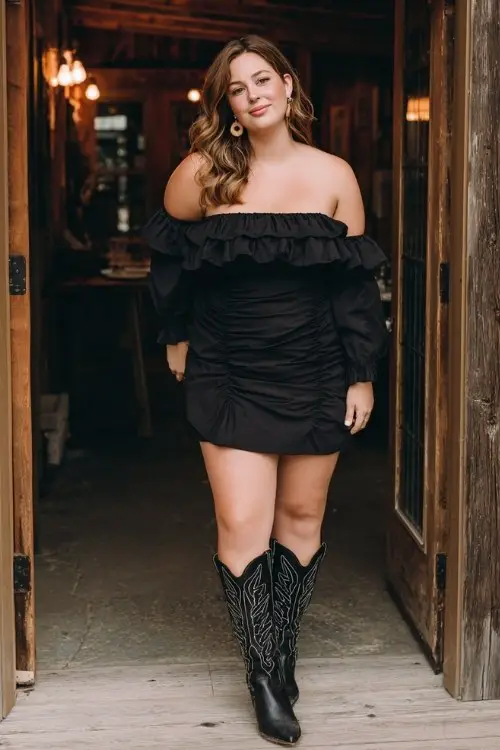 A plus-size woman wears a black off-shoulder mini dress with ruffle detail and tall black cowboy boots