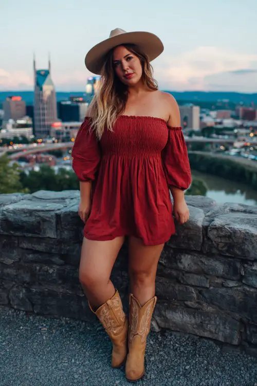 A plus-size woman wears a red off-the-shoulder smocked dress with tan cowboy boots and a wide-brim hat