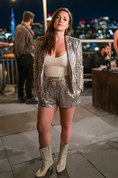 A plus-size woman wears a sequined blazer with matching tailored shorts and a simple fitted top, paired with sleek ankle boots