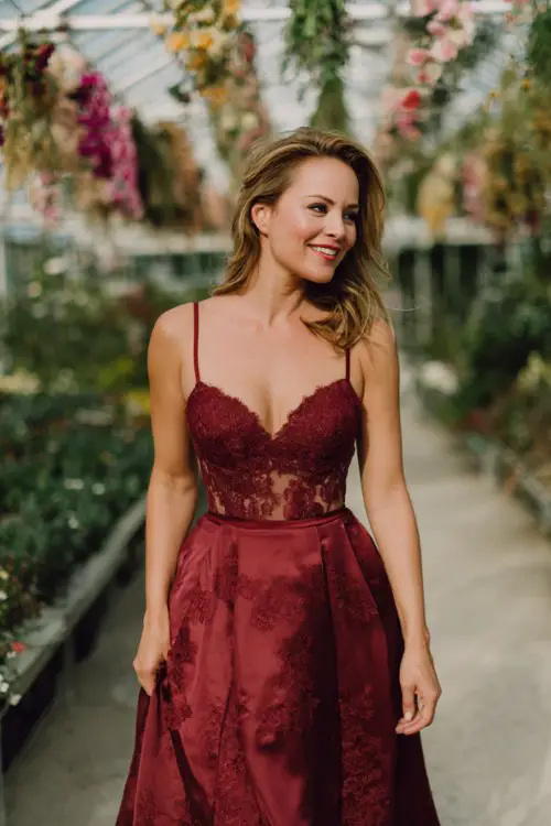 A woman over 40 wears a deep red A-line midi dress with a sweetheart neckline and a sheer lace overlay