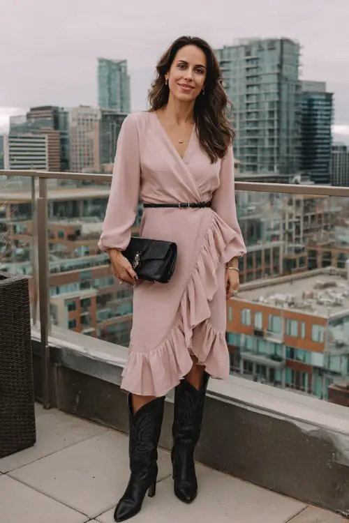 A woman over 40 wears a pink ruffle-hem midi dress with a belted waist and sleek black cowboy boots