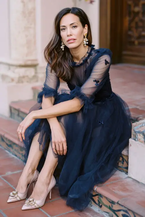 A woman over 40 wears a sophisticated navy tulle tea-length dress with sheer sleeves and subtle embroidery