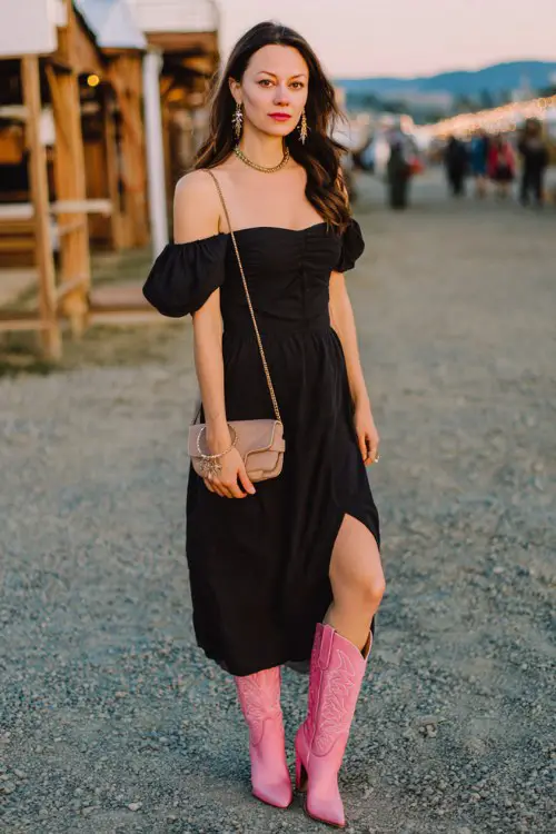 A woman wears a black off-shoulder dress with a flowy silhouette and pink cowboy boots, styled with statement jewelry and a structured bag (2)