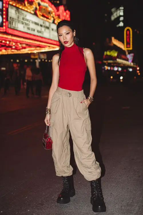 A woman wears a bold red fitted top with relaxed cargo pants and sleek platform boots, styled with stacked bracelets and a compact handbag