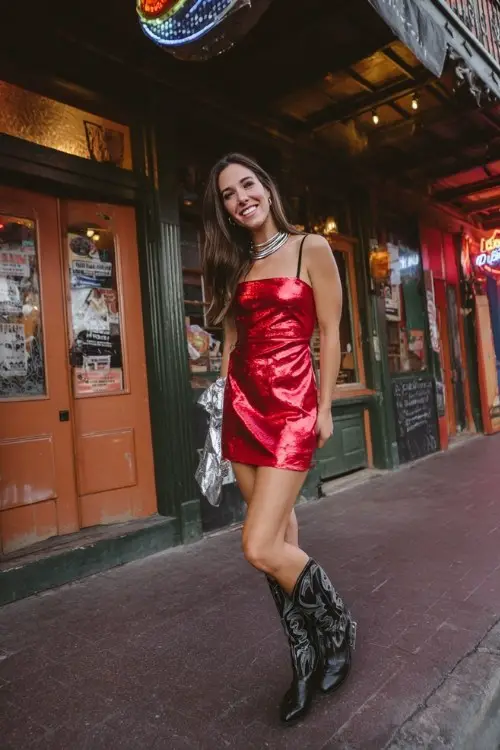 A woman wears a bold red mini dress with silver accessories and shiny black boots